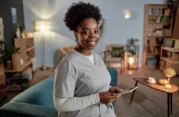 Smiling female home caregiver holding a tablet in a cozy living room.