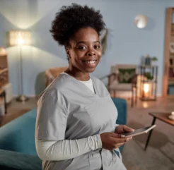 Smiling female home caregiver holding a tablet in a cozy living room.