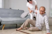 Caregiver assisting elderly man after a fall at home, highlighting fall prevention for seniors.