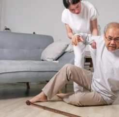 Caregiver assisting elderly man after a fall at home, highlighting fall prevention for seniors.