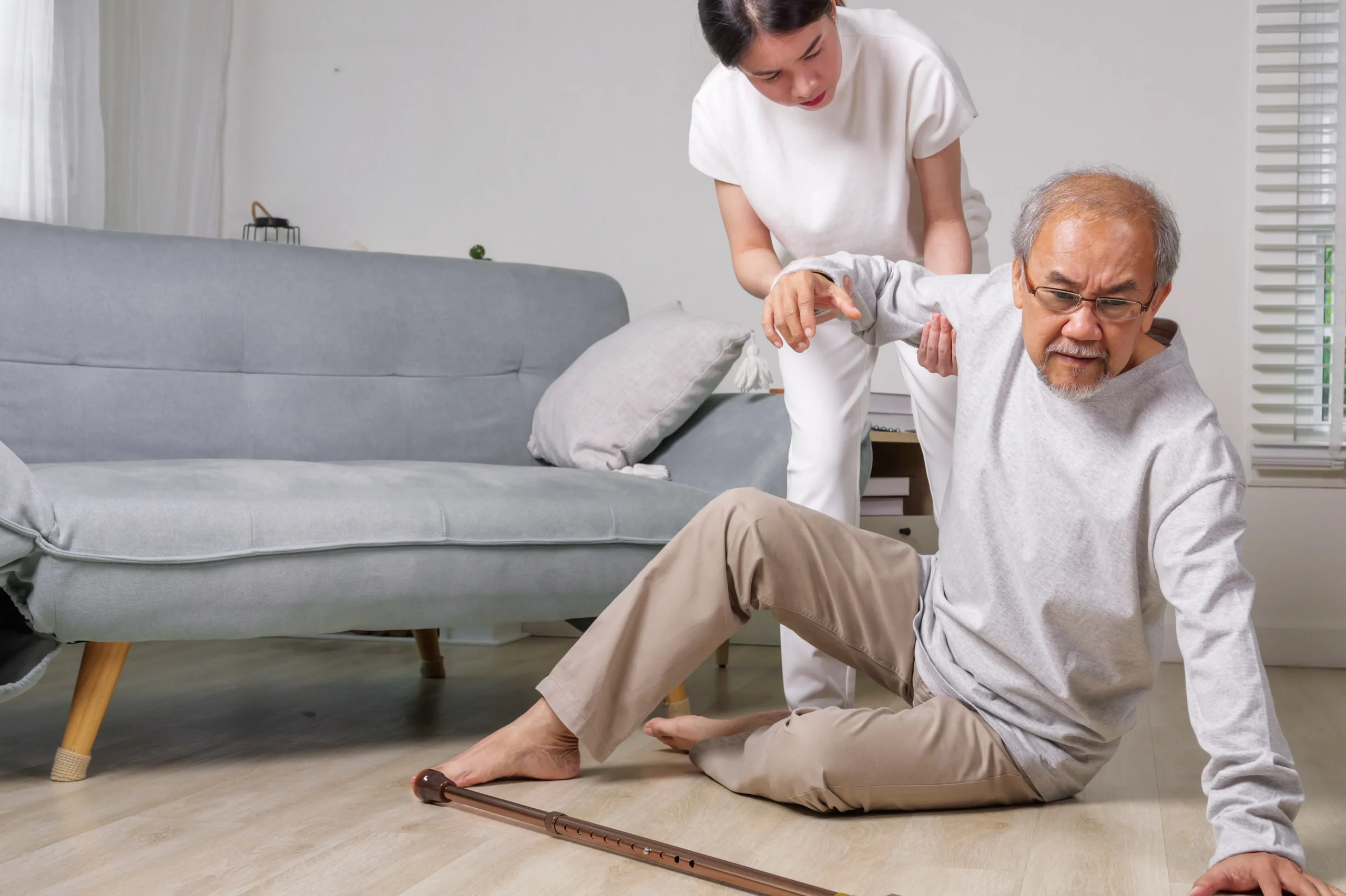 Caregiver assisting elderly man after a fall at home, highlighting fall prevention for seniors.