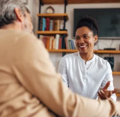 Female companion smiling and conversing with an elderly man in a cozy living room, offering emotional support and friendly conversation.