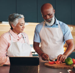 Older couple cooking with fresh vegetables and using a tablet for healthy meal ideas
