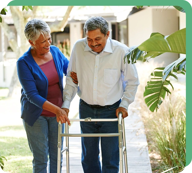Elderly couple walking outdoors; woman smiling, supporting man using walker